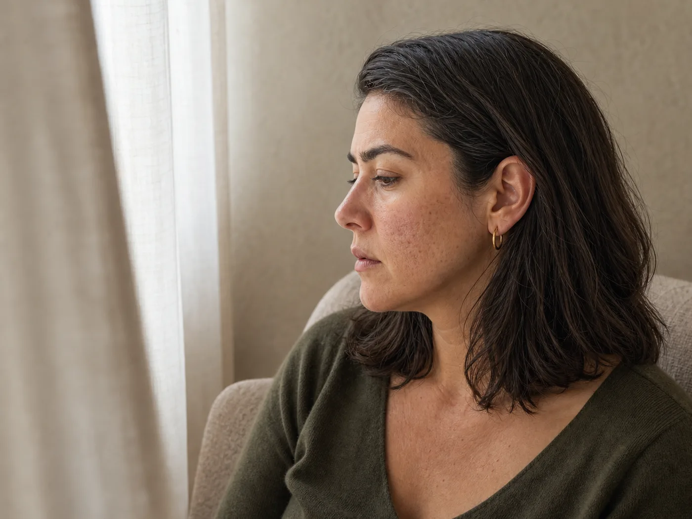 Woman in profile by a window with visible post-acne marks and natural skin texture